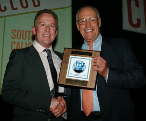 Former Los Angeles Press Club President, Bill Rosendahl, presents Collins with a "cheeseboard" slang for the First Place plaque that winners take home from the annual gala.